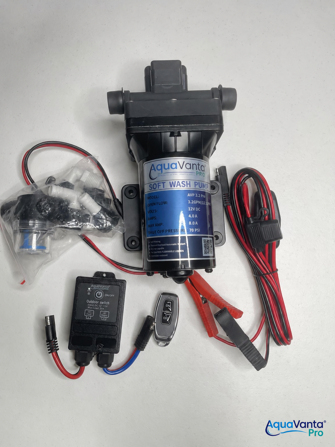 A black AquaVanta soft wash pump kit with a blue label, shown with wiring harnesses, a small black control module, a key fob, and a plastic-wrapped fitting on a white background.